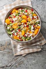 Quinoa salad with spinach, feta, tangerines, pomegranate, and pistachios, close-up in a bowl on the table. Vertical top view from above