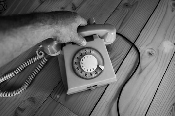 Monochrome image, caucasian man using an old, stationery ,rotary aged , vintage telephone from the 1980's.