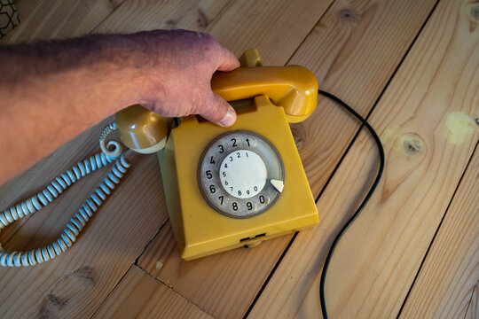 Caucasian man using an old, stationery ,rotary  aged , yellow  vintage telephone from the 1980's.