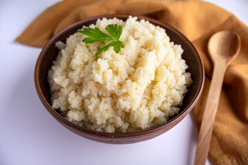 cooked couscous porridge in a clay bowl with parsley on a white background