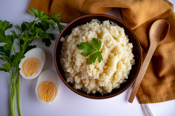 cooked couscous porridge in a clay bowl with parsley on a white background