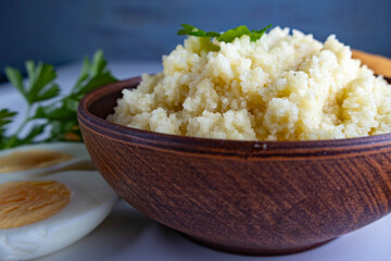 cooked couscous porridge in a clay bowl with parsley on a white background