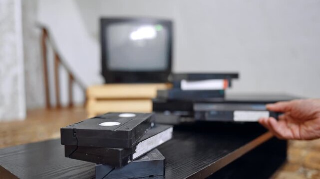 Pile of VHS cassettes on the desk. Male hand puts the cassette into the player and presses the button.