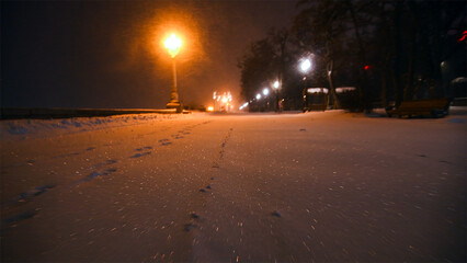 Fabulous view of the snow-covered city park at night, with trees in the snow, cozy warm light of lanterns.