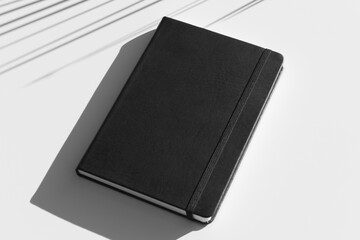 Black hardcover notebook mockup, shadow overlay, sunlight