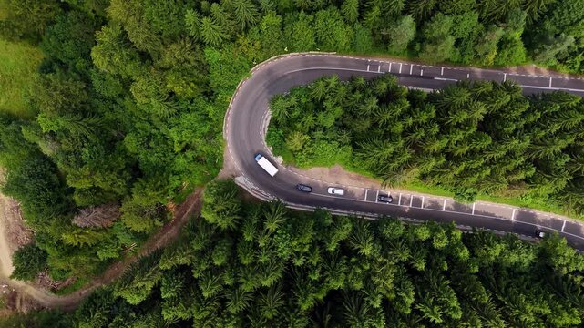 Sharp mountain road turn in green forest, Romania. Aerial top-down view of a sharp road turn surrounded by dense pine forest in the Carpathian Mountains of Romania.