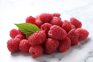 Delicious fresh ripe raspberries with green leaf on white marble table, closeup