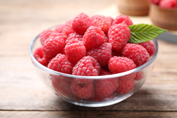 Delicious fresh ripe raspberries in bowl on wooden table, closeup