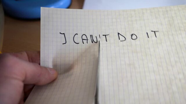 Caucasian man cutting in half a piece of paper with I can't do it note to reveal the I can text.