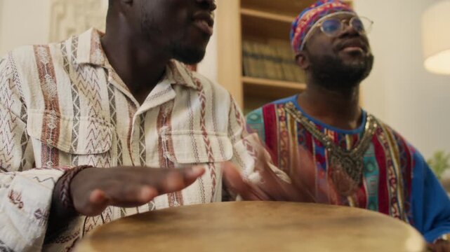 Low angle tilt down view of two African American young male friends playing goblet drums during home Kwanzaa celebration