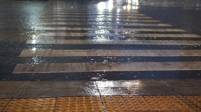 Motorbikes and cars pass over a wet pedestrian crossing during rain at night, traffic at night with city lights