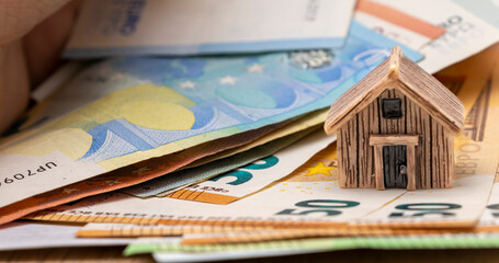 A miniature wooden house placed on a stack of euro banknotes represents real estate investment and mortgage concepts, highlighting financial planning for homeownership.