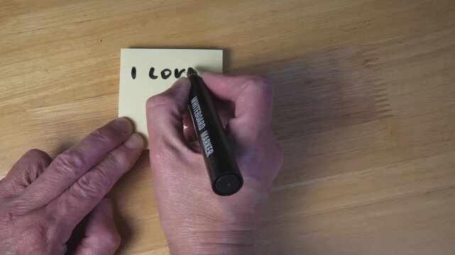 Hands Writing &ldquo;I Love You X&rdquo; on Yellow Post-It Note Close-Up