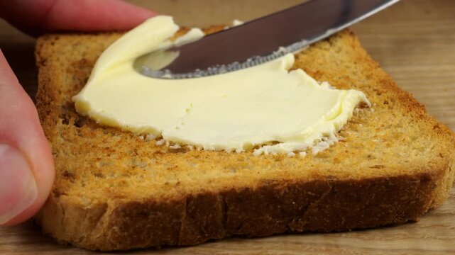 Grease a slice of toasted bread with butter using a knife.