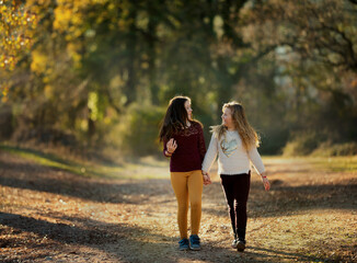  Two young girls walk hand in hand on a forest path, enjoying each other's company. They smile...