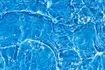 Blue water with ripples on the surface. Defocus blurred transparent blue colored clear calm water surface texture with splashes and bubbles. Water waves with shining pattern texture background.