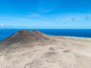 Aerial view of volcanic cones and arid landscape on La Graciosa Island, Canary Islands, with distant views of surrounding islands and the Atlantic Ocean.
