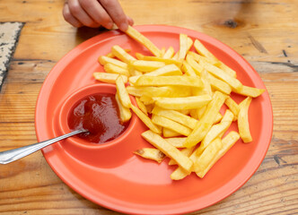 Crunchy French fries served with ketchup on a bright orange plate during a casual dining experience