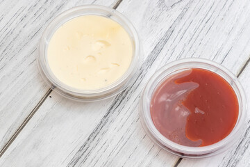 Two containers filled with sauce, one creamy and light, the other rich and reddish-brown, placed over a rustic wooden background, ideal for culinary presentations.