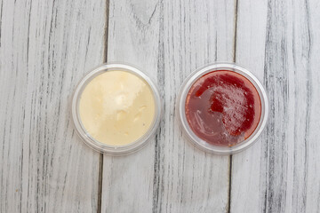 Two containers with sauces placed on rustic wooden background, featuring creamy mayonnaise and tangy ketchup. Perfect for culinary presentations or food photography.