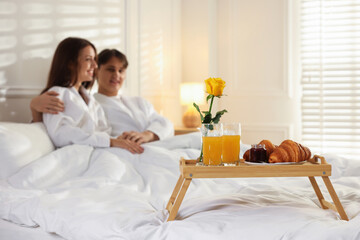 Tray with delicious breakfast on bed and happy couple enjoying their stay at hotel room, selective focus