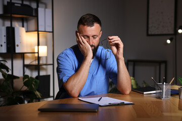 Fototapeta premium Tired doctor at table in clinic during night shift