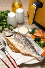Tasty grilled fish, vegetables, sauce and air fryer on wooden table, closeup