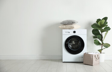 Washing machine, clean laundry and houseplant near white wall indoors. Space for text