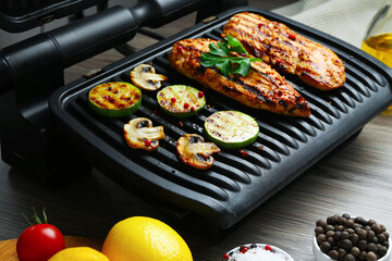 Electric grill with tasty chicken fillet, mushrooms, spices and products on wooden table, closeup
