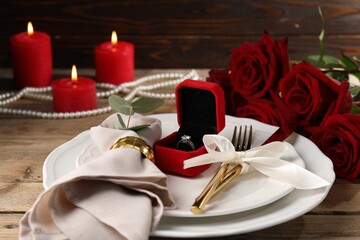Romantic place setting. Box with engagement ring, plates, cutlery, napkin, rose flowers and burning...