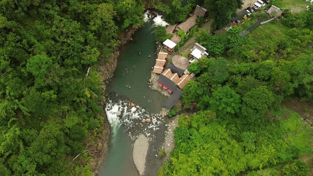 Slow forward aerial shows an emerald mountain river with rapids, a sandbar and a clear pool below nipa huts at Tampisaw River & Eco Park, Napsan, Puerto Princesa, Palawan, Philippines.