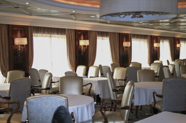 Formal elegant restaurant dining room onboard luxury cruiseship or cruise ship liner with set tables, ocean views and impressive interior inside architecture chandelier