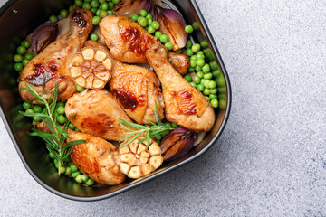 Air fryer basket with grilled chicken drumsticks, spices and green peas on grey table, top view. Space for text