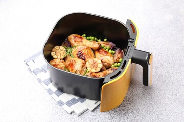 Air fryer basket with grilled chicken drumsticks, spices and green peas on grey table, closeup