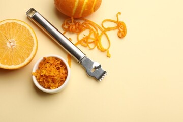 Orange zest, fresh fruits and zester tool on beige background, flat lay. Space for text