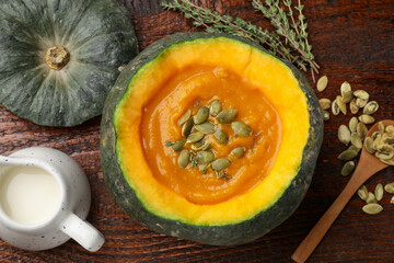 Tasty pumpkin cream soup with seeds and thyme served in pumpkin on wooden table, flat lay
