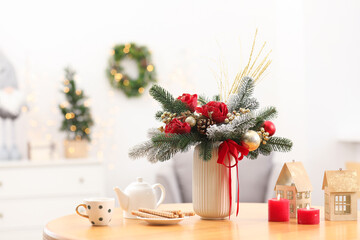 Beautiful composition with fir tree branches in vase, tea, treats and winter decor on wooden table against blurred lights, space for text. Bokeh effect