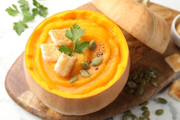 Tasty pumpkin cream soup with seeds, parsley and croutons served in pumpkin on white table, closeup