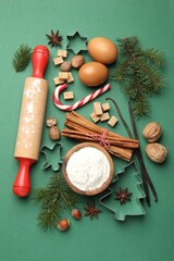 Christmas composition with cookie cutters, fir tree branches and spices on green background, flat lay