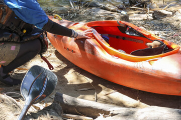 Focused person preparing an orange kayak and paddle on sunny riverbank. Outdoor activity for kayaking adventure, perfect for sport, recreation, and healthy lifestyle
