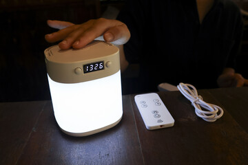 Hand touching glowing portable lamp with digital clock on dark table. cozy night light creating warm, calm, and relaxing atmosphere for peaceful evening at home