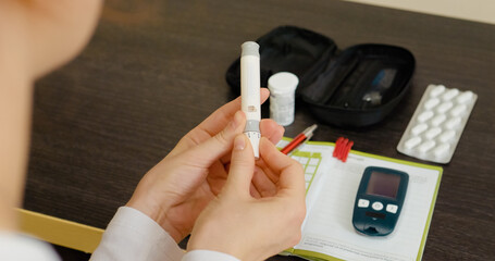 A woman uses a pen to prick her finger, testing her blood sugar level with a glucometer and ensuring her health management for diabetes.
