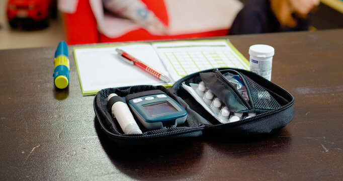 A glucometer set along with medication and a notebook placed on a table. It highlights the importance of monitoring blood sugar levels, recording data, and staying organized in diabetes management. - Powered by Adobe