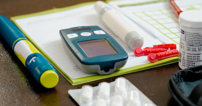 A person uses a glucometer to monitor blood sugar levels in their living room. Nearby, medications and a notebook are ready for recording test results and managing diabetes.