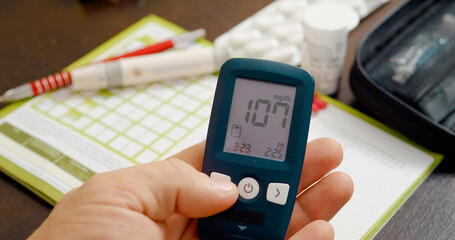 A man monitors his blood sugar levels with a glucometer and records the findings in his diary to manage his diabetes effectively.