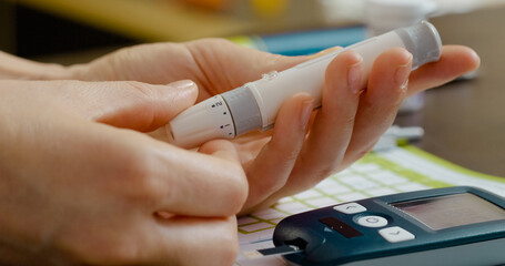 A woman carefully pricks her finger with a pen to check her blood sugar level with a glucometer. This routine is vital for managing diabetes effectively.