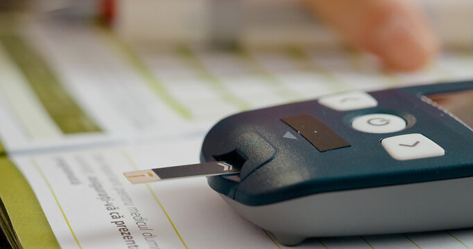 In a quiet setting, a woman carefully inserts a test strip into a glucometer to check her blood sugar level, monitoring her health for diabetes management.