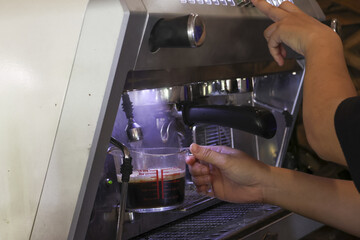 Professional barista making fresh hot coffee with an espresso machine in cafe. focused hand pours dark beverage into small glass cup for an energetic morning