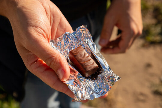 Hand is open and holding a chocolate bar or chocolate candy wrapped in shiny foil.