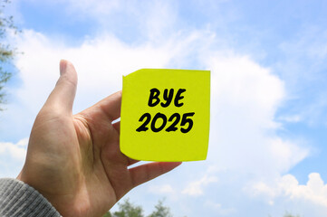 A hand holding a note with the words “Bye 2025” written against a clear blue sky. Saying Goodbye to the 2025 Year and Welcome a Fresh Start in 2026. End of the Year Reflection